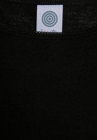 T-shirt nera con una texture liscia, dotata di un'etichetta a logo circolare sul colletto. Il tessuto sembra leggero e elasticizzato.