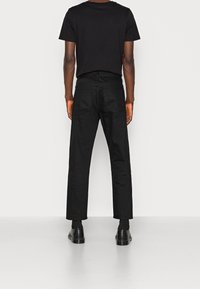Black cotton t-shirt paired with black, straight-leg trousers. Trousers feature two back pockets and are complemented by black shoes.