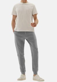 Szare bawełniane dresy z prążkowanymi mankietami, połączone z jasnobeżową koszulką. Strój ma klasyczny krój z okrągłym dekoltem.