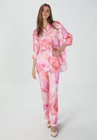 Blumiges Loungewear-Set bestehend aus einem lockeren, rosa Hemd mit Knöpfen und passender Hose mit großen weißen und rosa Blumenmustern.