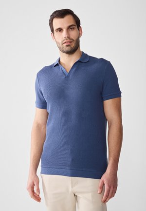 Polo de manga corta azul con textura acanalada y cuello en V. Presenta un cuello en contraste. Lleva puesto un pantalón de color claro.