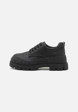 Chaussure noire montante à lacets avec une semelle épaisse et robuste et un col matelassé, conçue pour un usage décontracté ou streetwear.