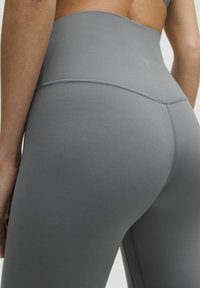 Sive legging visokog struka napravljeni od glatkog, rastezljivog materijala, sa bešavnom dizajnom i suptilnim šavovima.