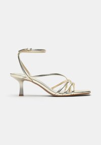 Guld sandaler med smalle stropper, lav kitten heel og ankelrem med spænde, elegant design, åben tå og tynde krydsede stropper foran.