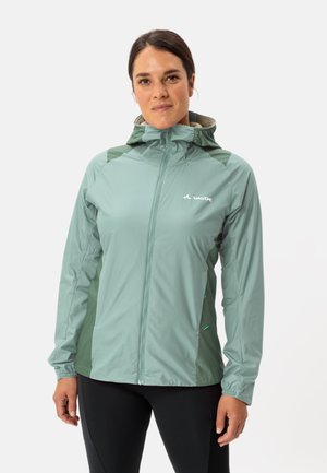 Giacca leggera di colore verde chiaro con cappuccio, chiusura a zip e tasche laterali. Presenta pannelli laterali di un verde scuro a contrasto e una texture liscia.
