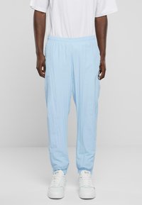 Light blue trousers with an elastic waistband, tapered fit, and subtle vertical texture. Paired with white sneakers.
