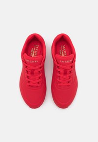 Rote Skechers Sportschuhe aus einem glatten, atmungsaktiven Material, mit runder Zehenpartie und Schnürdesign. Merkmale sind perforierte Akzente und ein gepolsterter Kragen.