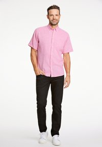 Korte mouwen, knoopsluiting overhemd in lichtroze, gemaakt van een geweven stof, gecombineerd met zwarte broeken en witte sneakers. Eenvoudig zakdetail zichtbaar.