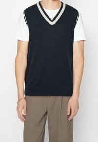 Granatowa bezrękawnikowa kamizelka z dekoltem w serek, z jasnoszarymi paskami wzdłuż linii szyi. Miękka tekstura i ściągacz na dole.