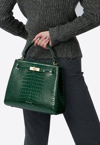 Zelená kabelka s krokodýlím reliéfem, strukturovaným tvarem, zlatým kováním a horním držadlem. Hladká textura a detail loga na spodní části.
