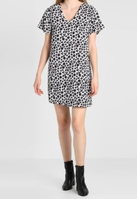 Mustavalkoinen kukkamekko, jossa on lyhyet hihat ja V-pääntie, löysä istuvuus ja kevyet kankaat. Yhdistetty mustiin nilkkasaappaisiin.