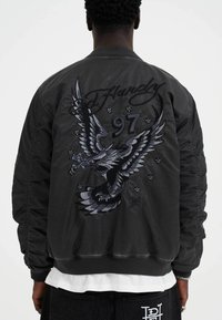 Black bomber jacket featuring an embroidered eagle design, the number "97," and "Ed Hardy" text in a contrasting color.