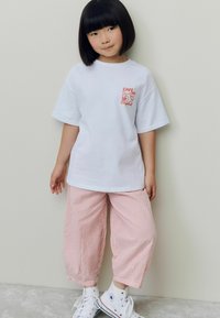 Vit bomulls t-shirt med röd café-grafik, matchad med röd och vit randiga lösa byxor och vita sneakers med blå detaljer.