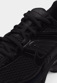 Chaussure de course Nike noire avec tige en mesh, semelle épaisse et lacets, gros plan sur les détails du côté et de la languette.