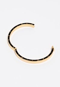 Pulsera de brazalete de metal en tono dorado con incrustación de esmalte negro que presenta letras doradas espaciadas formando la palabra "IMBAYOLA."