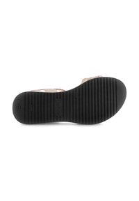 Black rubber sole of a sandal, featuring vertical ridges for traction. Light tan-colored upper visible, with adjustable straps for fit.