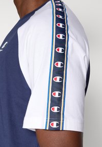 Κοντομάνικο μπλουζάκι σε ναυτικό μπλε και λευκό. Διαθέτει ριγέ πλαϊνή λωρίδα με λογότυπα σε κόκκινο, λευκό και μπλε. Μαλακό βαμβακερό ύφασμα, άνετη εφαρμογή.