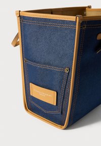 Modrá rifľová taška so svetlohnedým koženým lemovaním, predným vreckom a svetlohnedou koženou štítkom s nápisom "Gianni Chiarini Firenze" na bielom pozadí.