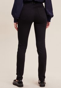 Jean skinny noir avec taille haute, doté de deux poches arrière et d'une texture lisse. Associé à de élégantes chaussures noires.
