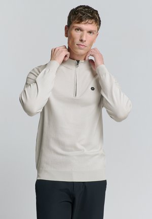 Beige zip-neck trui met lange mouwen, geribbelde manchetten en zoom, voorzien van een klein hexagonaal logo op de borst, gemaakt van zacht breimateriaal.