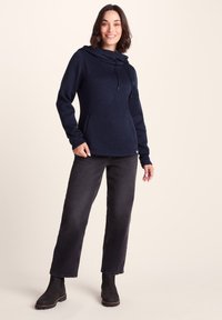 Navy blue pullover hoodie with a cowl neck, drawstring, and front pocket. Paired with black straight-leg jeans and ankle boots.
