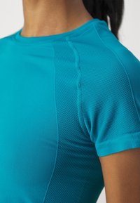 Maglietta sportiva turchese con pannello laterale testurizzato e design delle spalle senza cuciture. Tessuto morbido e elastico con una silhouette aderente.