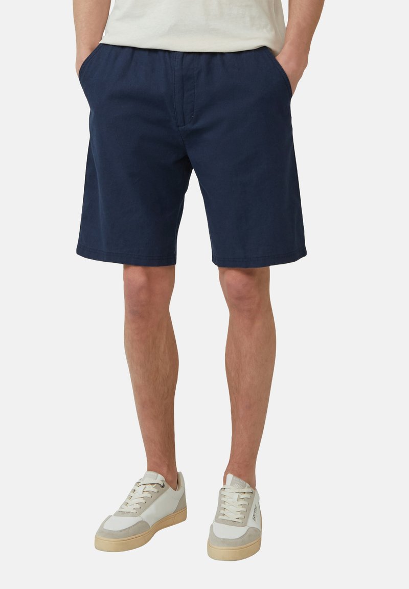 Pantaloni corti in cotone blu navy con vita elasticizzata, tasche laterali e una vestibilità rilassata. Indossati con sneakers di colore chiaro.