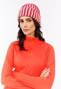 Gebreide beanie met rode en witte strepen, met een gestructureerde afwerking en een klein merklabel. Het model draagt een feloranje zip-up top.