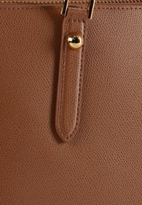 Καφέ δερμάτινη υφή με λείο φινίρισμα και χρυσό διακοσμητικό κουμπί. Διαθέτει ραμμένο λουράκι που συνδέεται με φερμουάρ κλεισίματος.