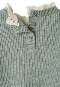 Grüner gerippter Stricktop mit einem weißen Spitzenkragen und zwei hellblauen Knopfverschlüssen am Hals. Weiche Textur mit ausgeprägtem Muster.