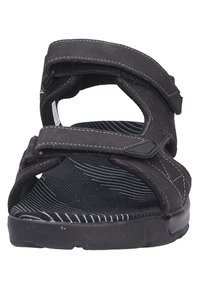 Sandalias negras con correas de velcro ajustables, suela negra texturizada y un sutil patrón de rayas blancas en la plantilla. Material suave con detalles de costura.