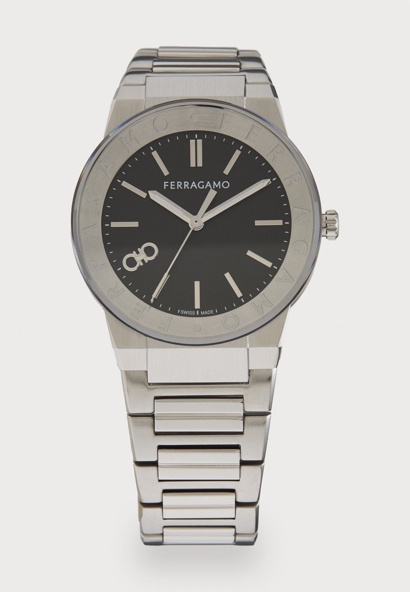 Sidabrinės spalvos nerūdijančio plieno laikrodis su juodu ciferblatu, išryškintais valandų žymenimis ir logotipu. Sujungta apyrankė ir apvalus korpusas.