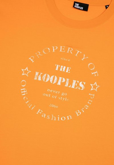 Oranje katoenen t-shirt met een ronde witte afbeelding waarin de merknaam "The Kooples" staat, sterren, en tekst in een verweerde stijl.