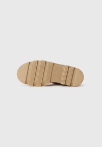 Semelle de chaussure en caoutchouc beige avec des rainures horizontales pour l'adhérence, dotée d'un bout arrondi et d'un logo en relief près du talon.
