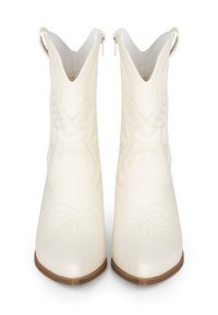 Botas de tobillo de piel blanca con punteras puntiagudas, diseño floral en relieve, superficie texturada y tiradores. Tacones de madera marrón, silueta estilizada.