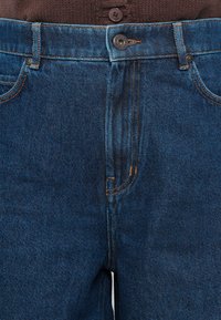 Jeans din denim de culoare albastru închis, cu închidere prin buton, detalii de cusături vizibile și un design clasic cu cinci buzunare.