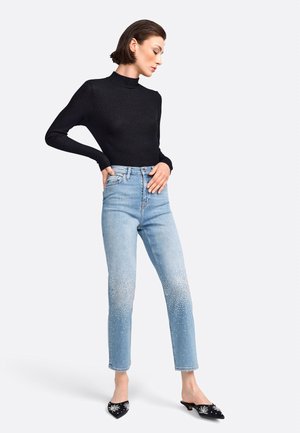 Schwarzes Langarm-Turtleneck-Oberteil, hellblaue hoch taillierte Jeans mit verstreuten Strassakzenten; kombiniert mit schwarzen, verzierten Mules.