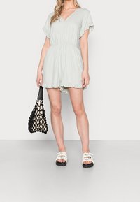 Světlé zelené dupačky s krátkými volánkovými rukávy, elastickým pasem a volánkovým lemem. Doplněné bílými sandály a černou síťovanou kabelkou.