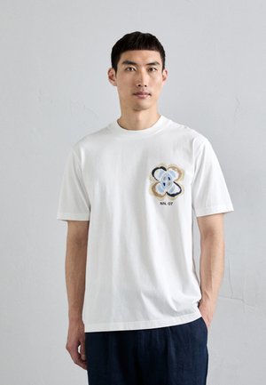 Hvid bomulds t-shirt med kortærmet design, prydet med et flerfarvet blomstermønster på brystet og teksten "NN. 07" nedenunder.