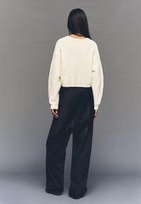 Kratki kremasti džemper s dugim, napuhanim rukavima, upareni s širokim crnim hlačama koje imaju poderani rub i mekanu teksturu.