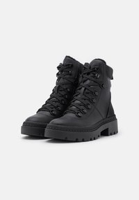 Bottines en cuir noir à lacets avec semelles en caoutchouc épaisses et cols rembourrés, sur fond blanc uni.