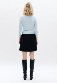 Himmelblaues Strickpullover mit einem strukturierten Muster, kombiniert mit einem dunkelblauen Rock. Schwarze kniehohe Stiefel runden das Outfit ab.