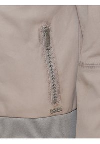 Hellbeige Lederjacke mit einem silbernen Reißverschluss, gerippten grauen Bündchen und einem kleinen Logotag am Saum. Glatte Textur mit subtilen Abnutzungserscheinungen.