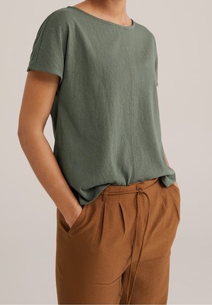 Vihreä lyhythihainen toppi pehmeästä, tekstuurilla varustetusta kankaasta; pyöreä pääntie, ilmava istuvuus. Yhdistetty ruskeisiin korkeavyötäröisiin housuihin, joissa on solmuseikka.