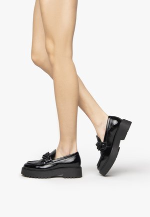 Black patent loafers with a chunky sole, bow detail, and smooth texture, showcasing a low-cut design and clean lines.