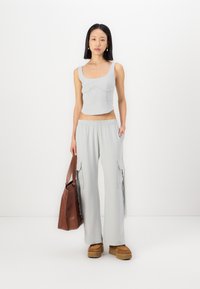 Lys grå crop-top med buet sømdetalj, kombinert med løstsittende lysegrå cargo-bukser med sidelommer og elastisk midje. Brun veske og plattformsko.