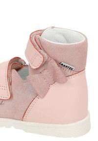 Hellrosa Knöchelstiefel mit einem strukturierten Textilobermaterial, Klettverschluss und einer Schleifenakzentuierung. Verfügt über eine weiße Gummisohle mit dezentem Branding.