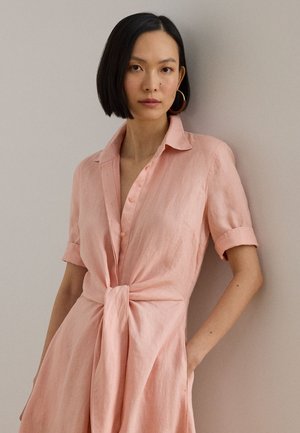 Różowa lniana sukienka koszulowa z krótkimi rękawami, zapinana z przodu na guziki, z detalem w postaci wiązania w talii. Lekka, fakturowana tkanina o luźnym kroju.