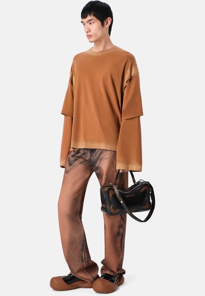 Oversized brązowy sweter z długimi rękawami, połączony ze wzorzystymi brązowymi spodniami. Czarna torba na ramię i brązowe buty dopełniają całość.