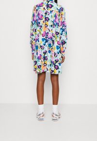 Färgglad blommig klänning med en blandning av rosa, blå och gula blommor på en ljus bakgrund, med långa ärmar och knäppt hals.